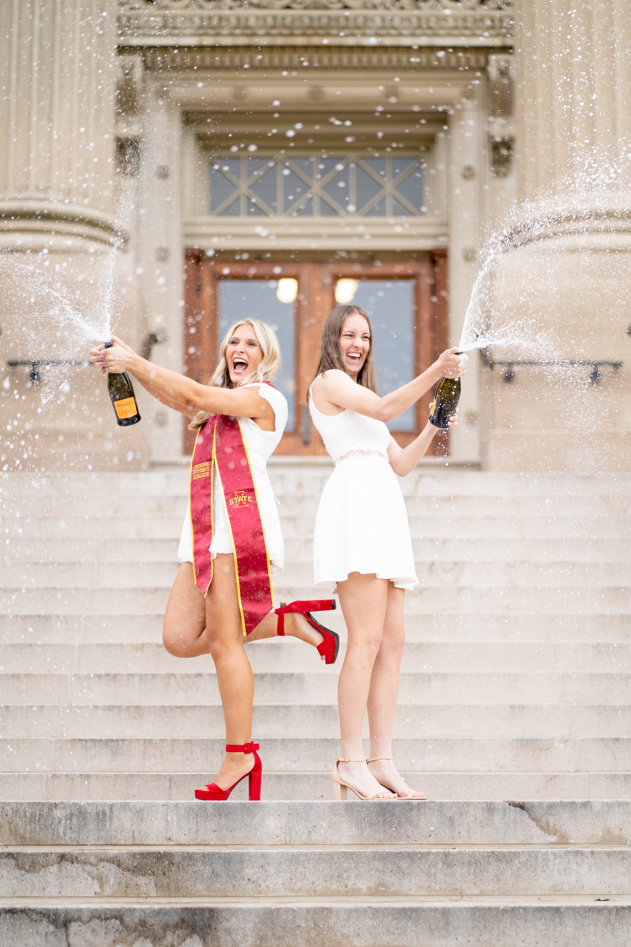 Two graduates spraying champagne together on the Iowa State campus steps