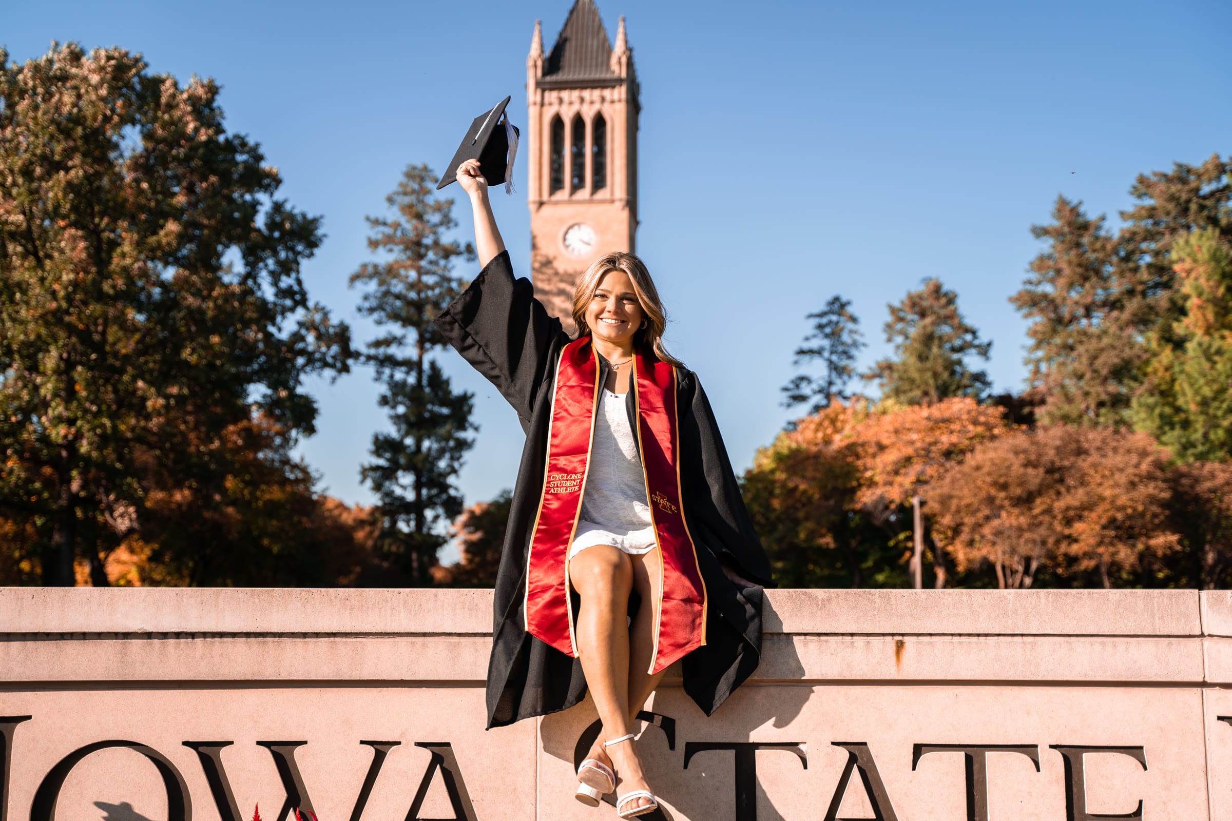 Graduate raising her cap in celebration in front of the Campanile