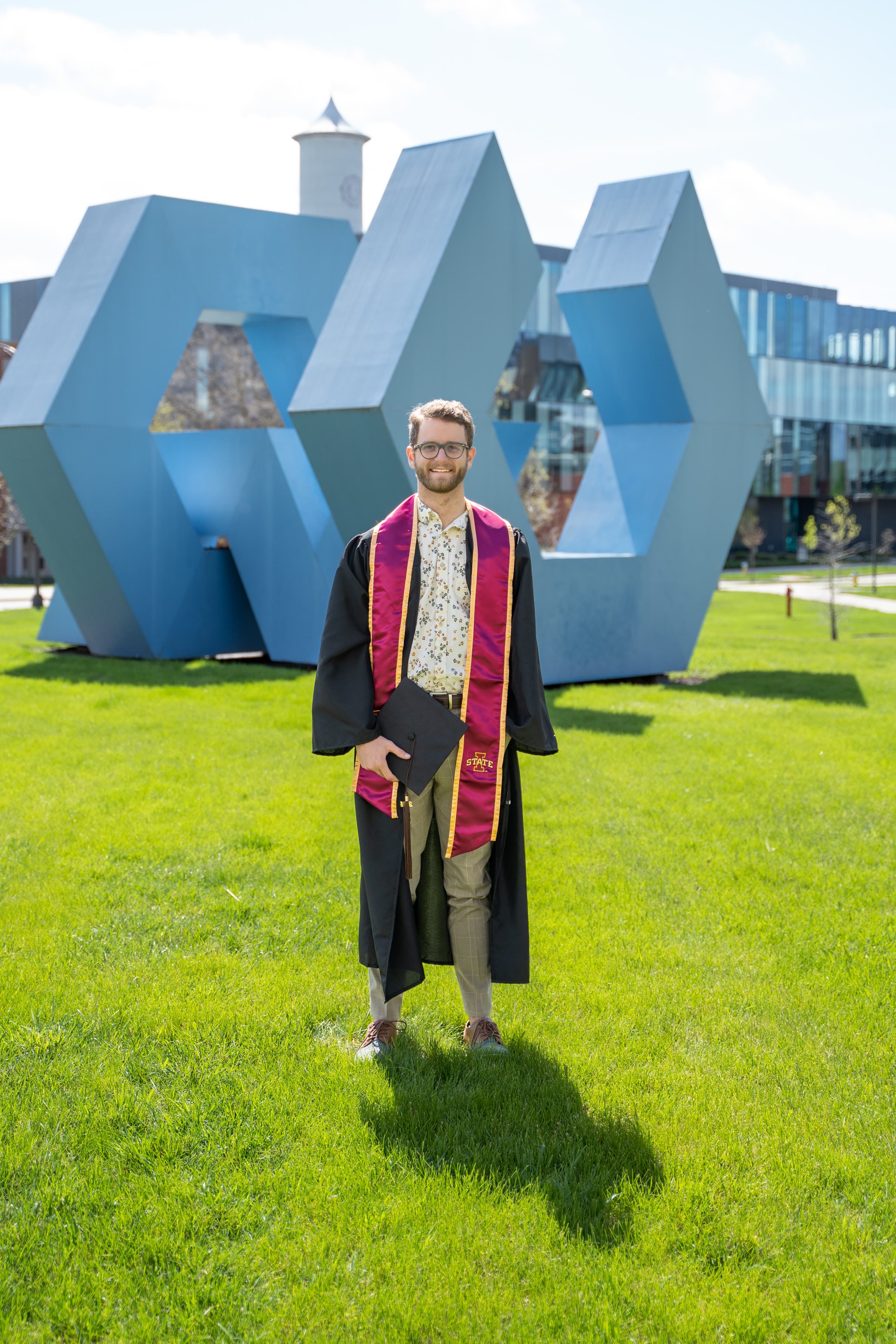 Graduate portrait in front of a large outdoor sculpture on campus