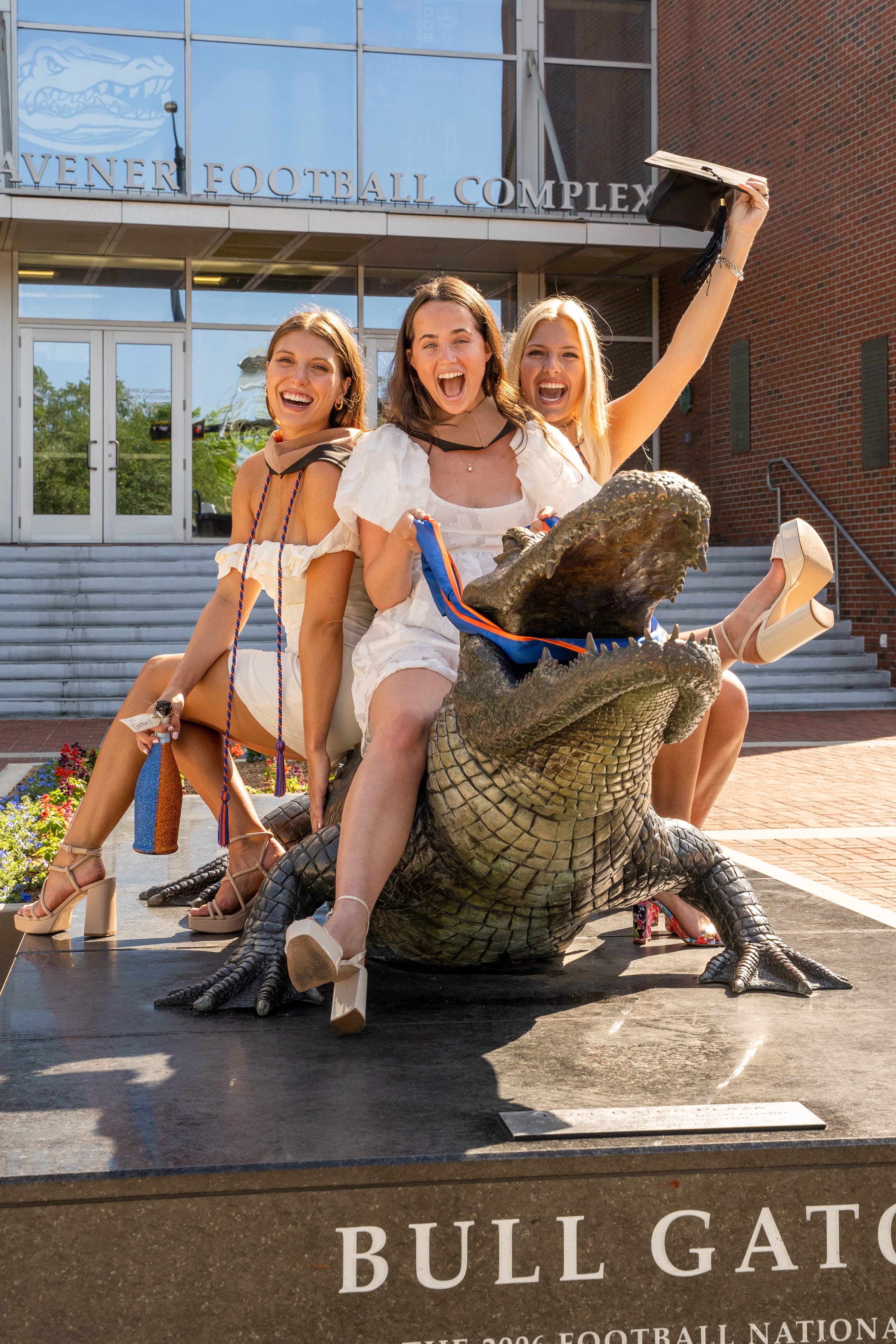 Three graduates celebrating together on a campus statue