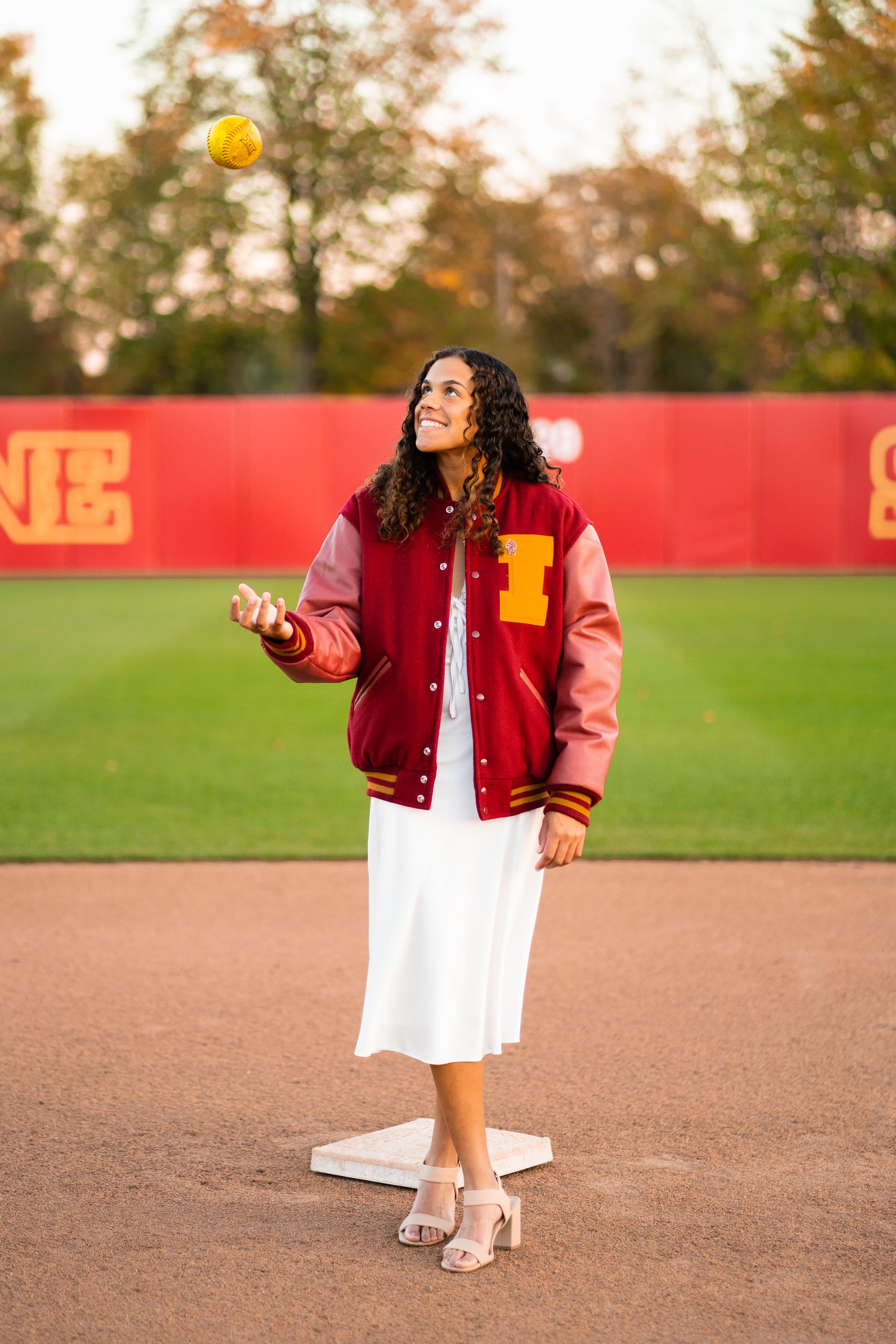 Senior softball athlete portrait tossing a softball in a letterman jacket
