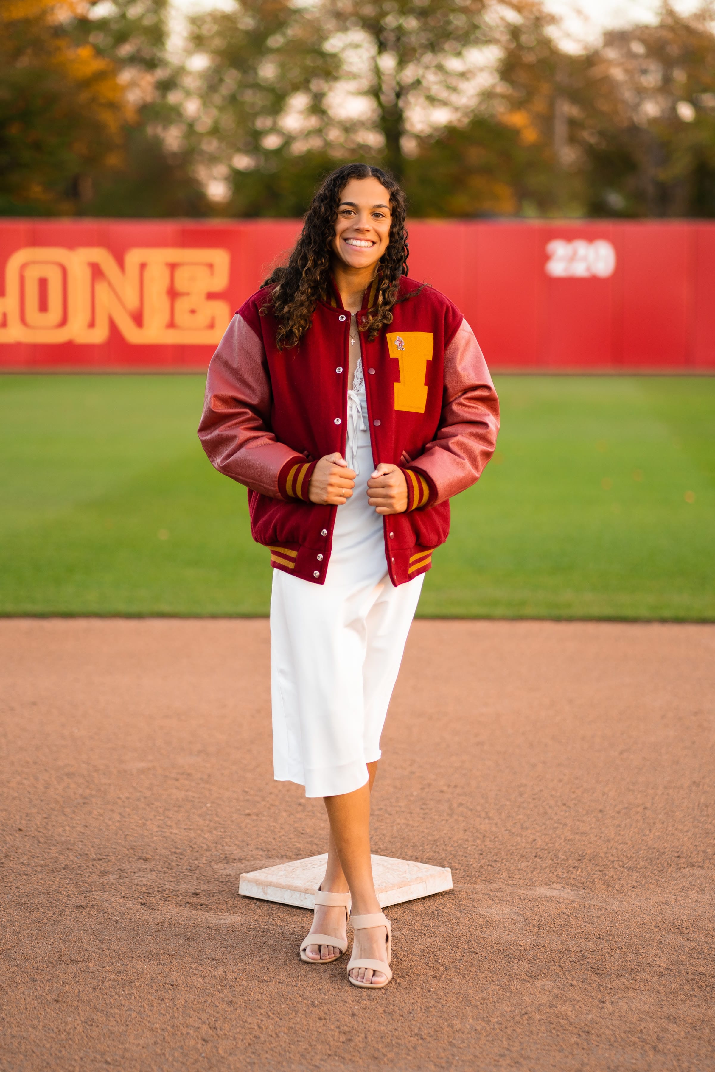 Senior athlete portrait in a varsity letterman jacket on a softball field